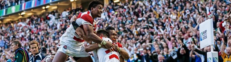 Japan's Karne Hesketh celebrates with team mates at the corner of a rugby pitch with cheering crowd in the background