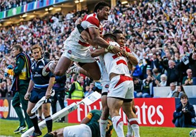 Japan&#39;s Karne Hesketh celebrates with team mates at the corner of a rugby pitch with cheering crowd in the background