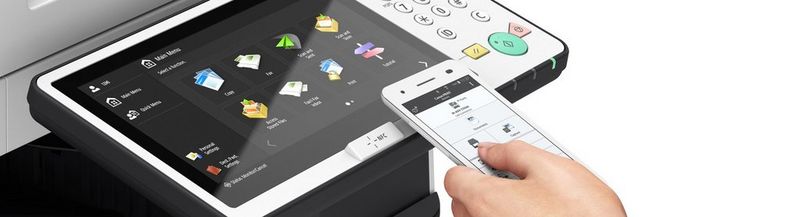 A hand holds a smartphone near the touchscreen of a Canon imageRUNNER office machine.