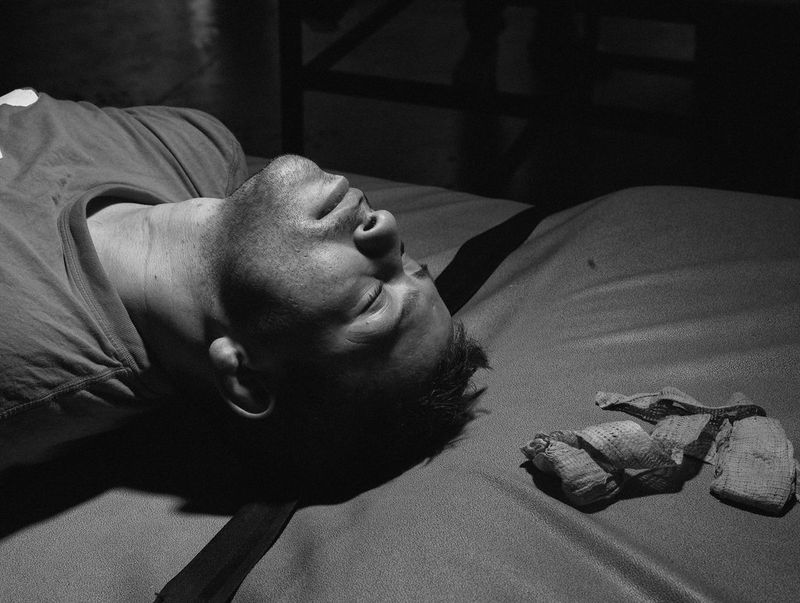 A close-up of a boxer lying on an exercise mat, with his hand bandages next to his head.