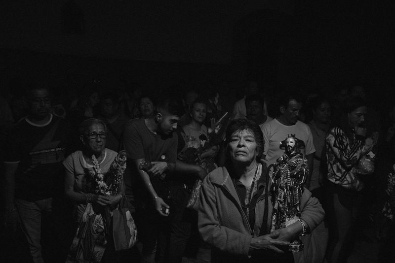 A crowd of worshippers at a religious festival, many of them carrying statues of a bearded saint.