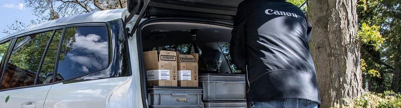 A Canon Service Engineer in a branded jacket unloads their equipment from the back of a white estate vehicle.