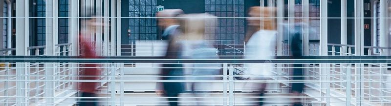 Blurred figures crossing an office walkway.