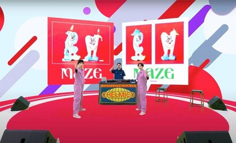The two women in lilac jumpsuits now stand in the same position in the same studio, but with red, grey and purple patterns on the wall behind them, and two banners with the word ‘maze’ on them. © Warner Music Japan Inc. 