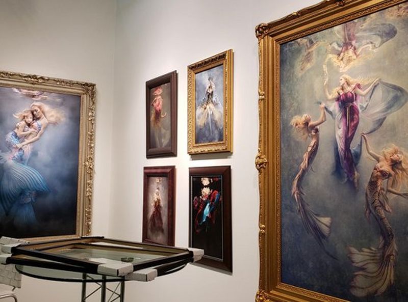 Large prints of Cheryl’s work, hanging in beautiful decorative frames. A table with some frames sits in front of them.