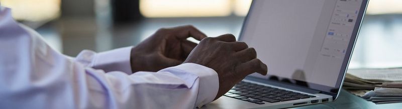 The arms and hands of a man in a white shirt, typing on a laptop.