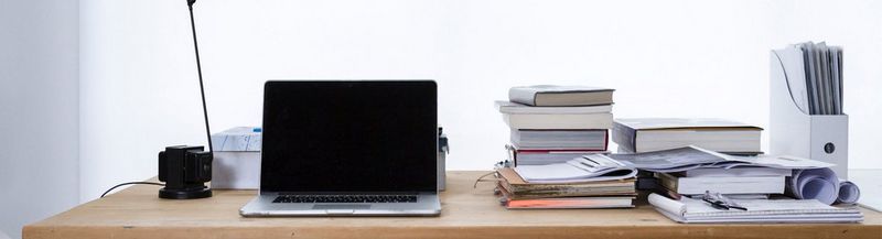  A wooden desk, with a stack of piled books beside a laptop.