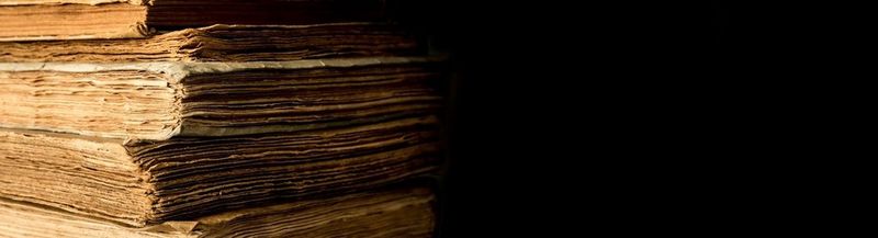 On the left, a stack of very old books, viewed from the leaves not spine. On the right, a black background.