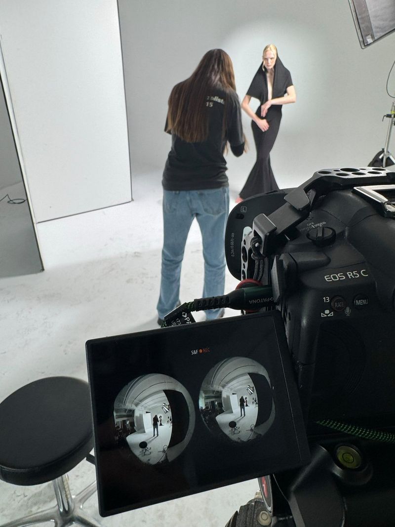 A behind the scenes image of Agata Serge photographing a model, in the foreground a Canon EOS R5 C camera with the output from the RF 5.2mm F2.8L DUAL FISHEYE lens visible on the flip-out screen. 