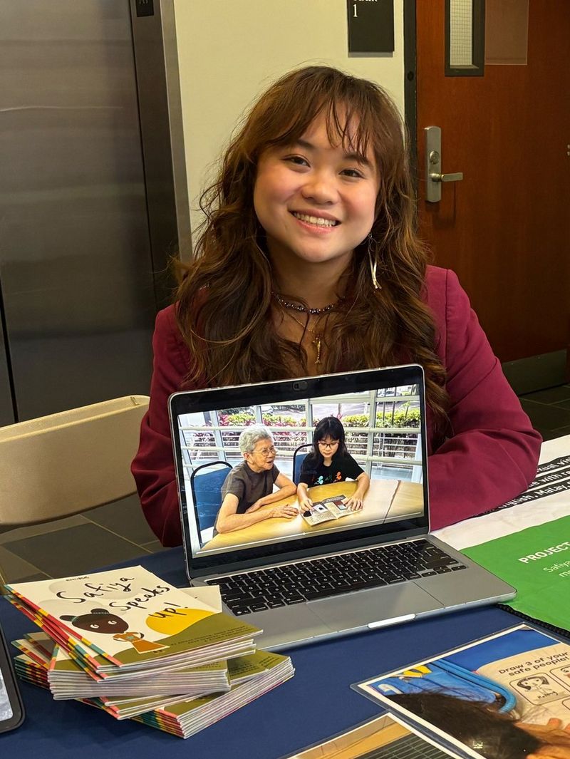 Allison Choong sits at a desk with a laptop, smiling.