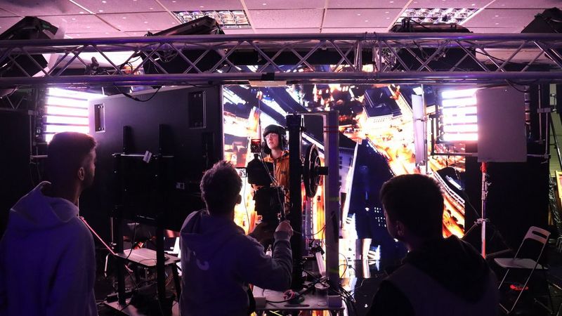 A behind-the-scenes shot of Pozzy’s music video, where he stands in front of large LED screen displaying a bright city street at night.
