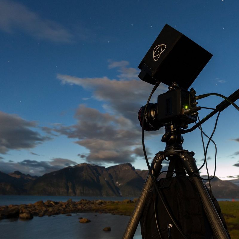 A Canon ME20F-SH cinema camera attached to a tripod beside a mountain lake.