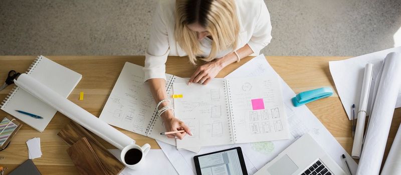 Three women and a man dressed in business casual sit around a table in a partitioned office, looking at a laptop screen.