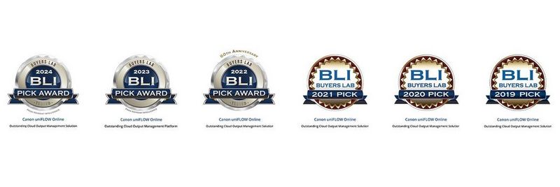 Seven people sit at two long desks facing each other in a sparsely furnished office with concrete walls, wooden floors and big windows at the far end. 