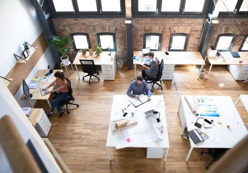 Wide overhead shot of creative office layout with people working at desks adorned with computers, lamps and brochures.
