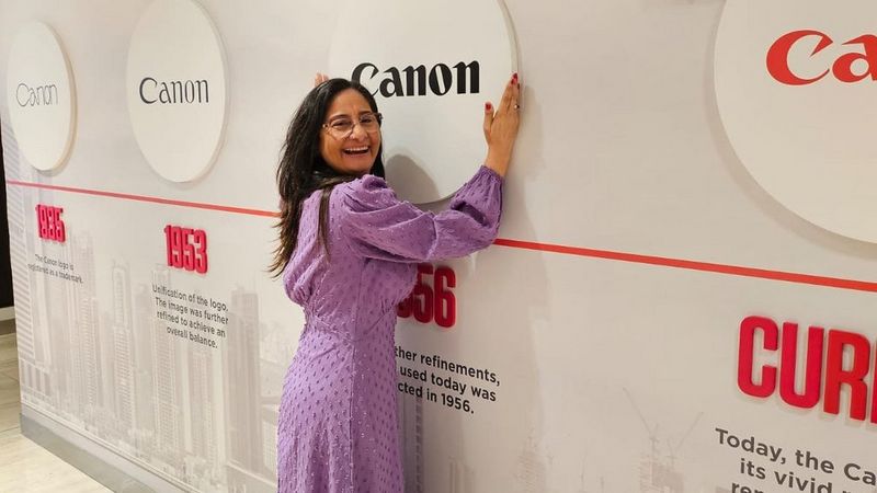 A happy woman stands in front of the Canon logo.