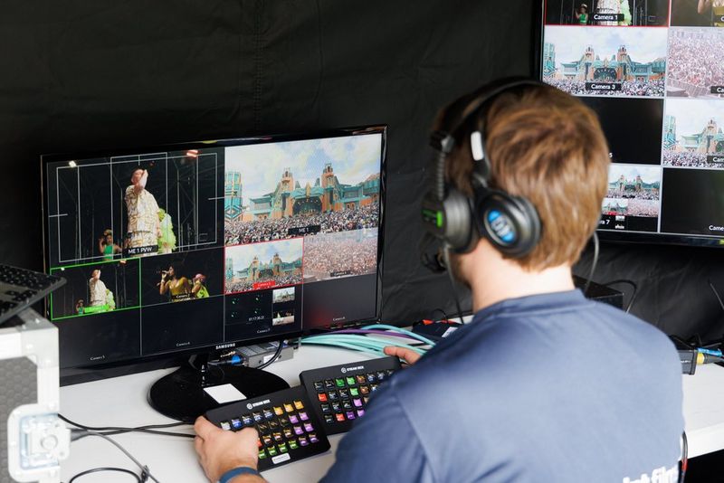 Een persoon staat voor een beeldscherm waarop de feeds van meerdere camera's te zien zijn en bedient een controller voor meerdere camera's.