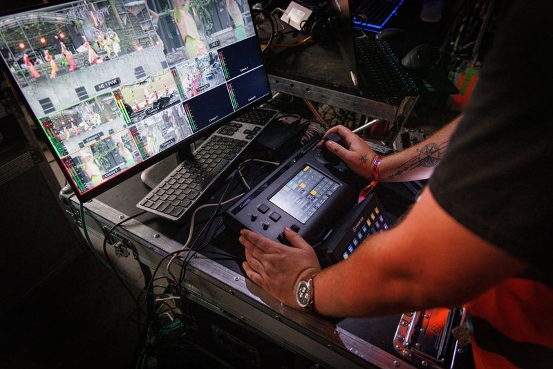A technician’s hands operating a Canon RC-IP1000 controller in front of a screen showing multiple camera feeds.