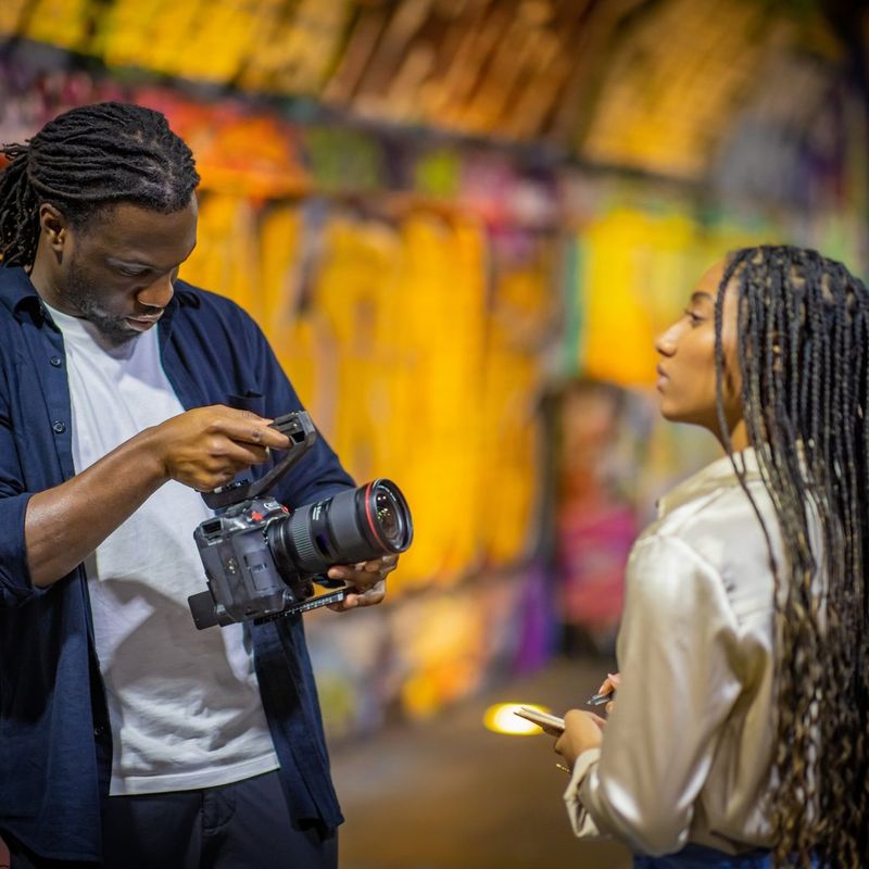 Een man houdt een Canon EOS C70-camera vast en filmt een vrouw in een tunnel vol graffiti.