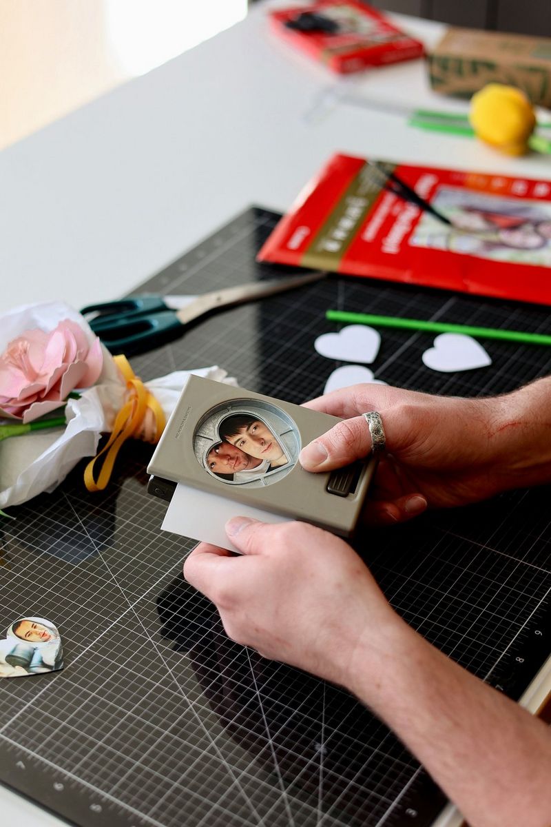 A pair of hands uses a hole punch to cut out heart-shaped photos. On the table below are a pair of scissors, a cutting board and a pack of Canon paper.