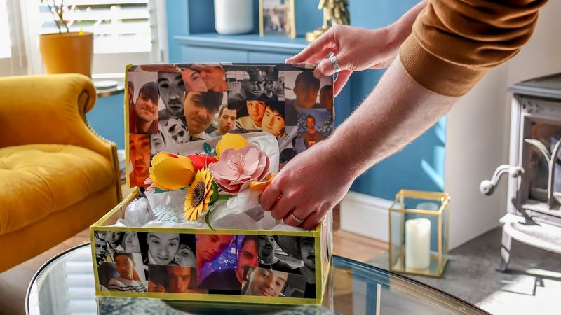 A pair of hands places a papercraft flower bouquet, created with a template from Canon Creative Park, into a hand-crafted box decorated with découpage photographs.