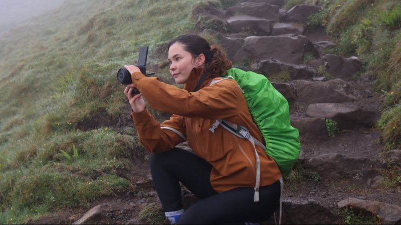 Vlogger Niamh Mackinnon crouches on a stone step on a misty mountain on the Isle of Skye, filming a vlog with the Canon EOS R50 V.
