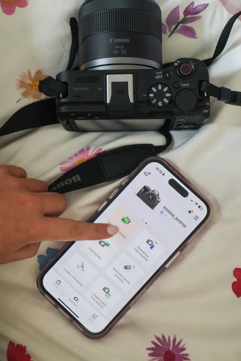 Vlogger Niamh Mackinnon’s finger taps the screen of a smartphone running the Canon Camera Connect app, controlling a Canon EOS R50 V camera alongside.