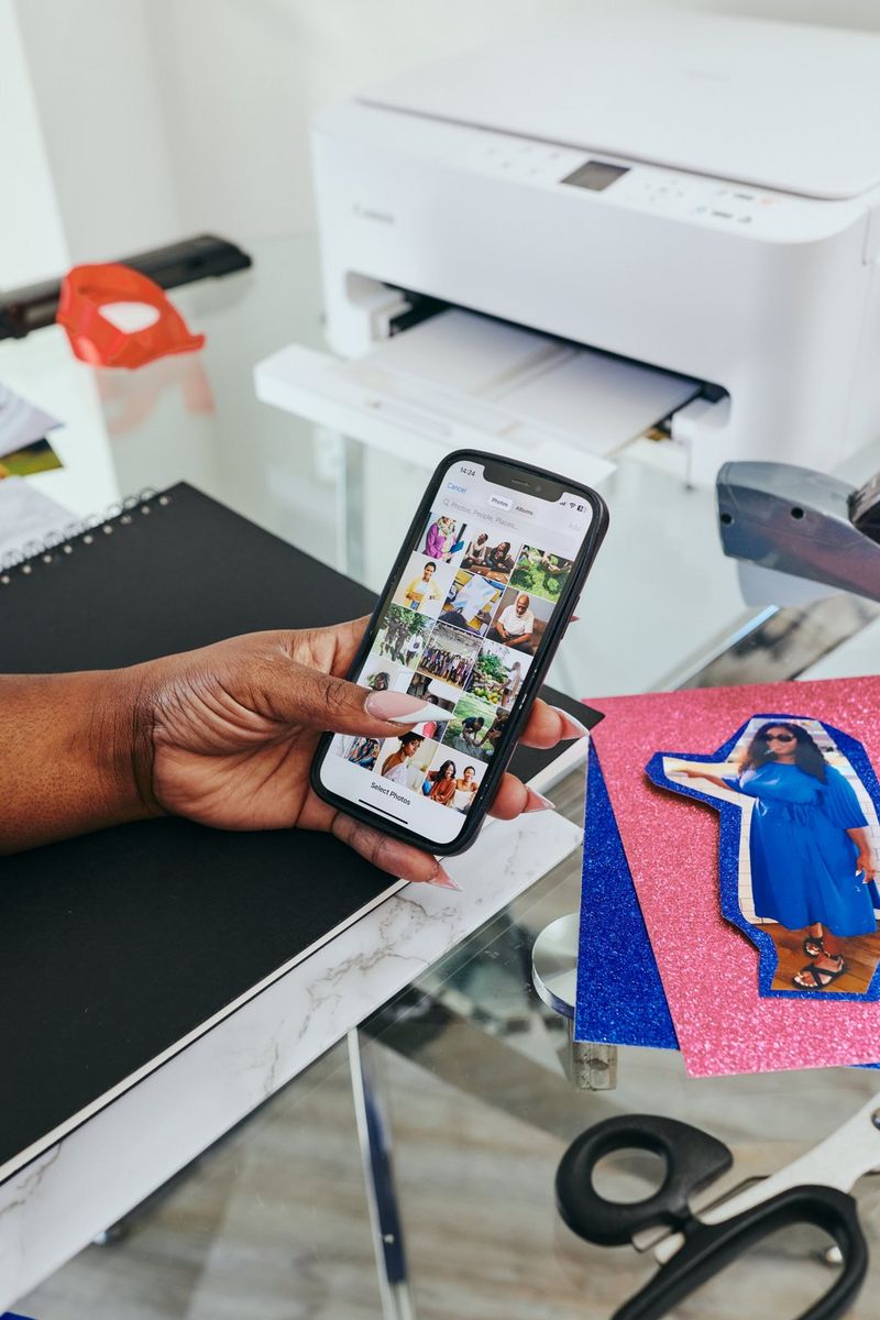 En bruger vælger billeder, der skal printes, fra en skærm fuld af billeder ved hjælp af Canon PRINT-appen på en smartphone, med en Canon PIXMA-printer i baggrunden.