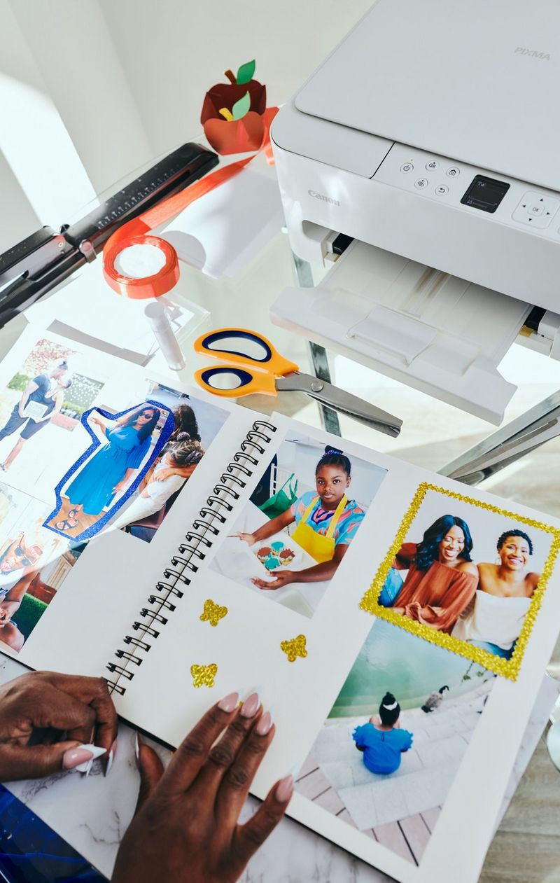 To sider i et håndlavet fotoalbum, der er dekoreret med en udklippet figur, en farvet papirramme omkring ét billede og farverige former, der er indsat på siden. Der står en Canon PIXMA-printer på bordet bagved.