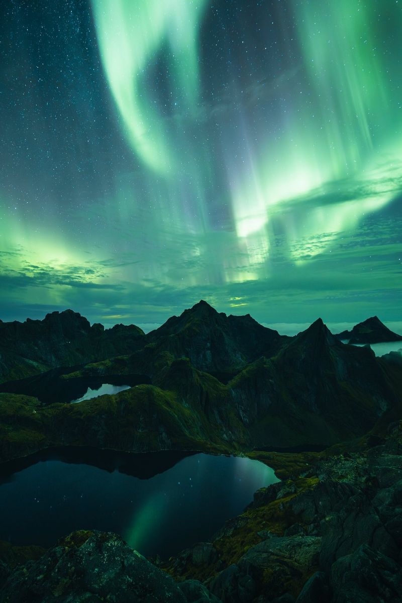 The Northern Lights appear as shimmering green streaks in the sky above the Lofoten Islands in Norway. Night sky photo taken with a Canon EOS R3 camera and Canon lens by Manuel Dietrich.
