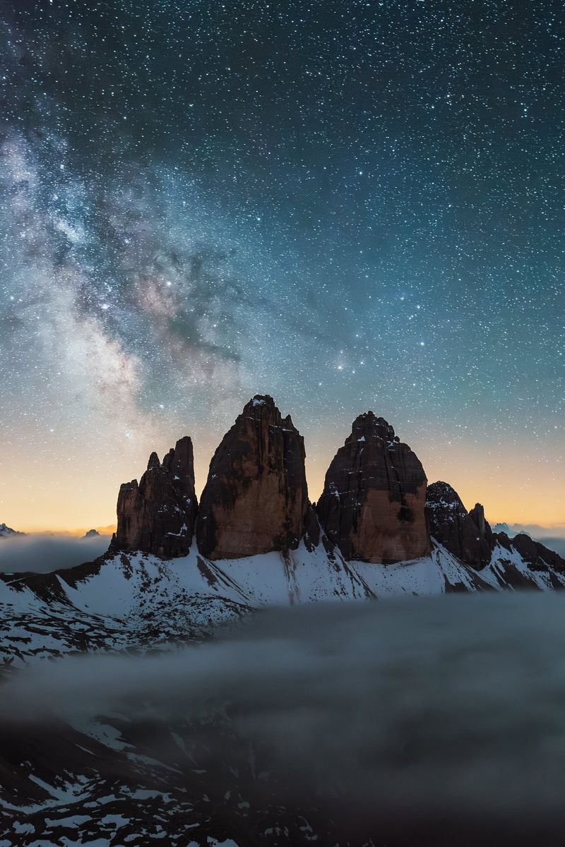 The Milky Way photographed in the skies above the Tre Cime di Lavaredo in the Italian Dolomites, with the foreground landscape covered by fog. Night sky photo taken with a Canon EOS R3 camera and Canon lens by Manuel Dietrich.