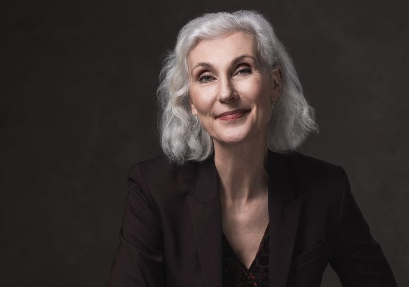 A painterly portrait photo of a lightly-smiling woman with silver-grey hair, taken on a Canon EOS R5 with a Canon RF 100mm F2.8L MACRO IS USM lens.