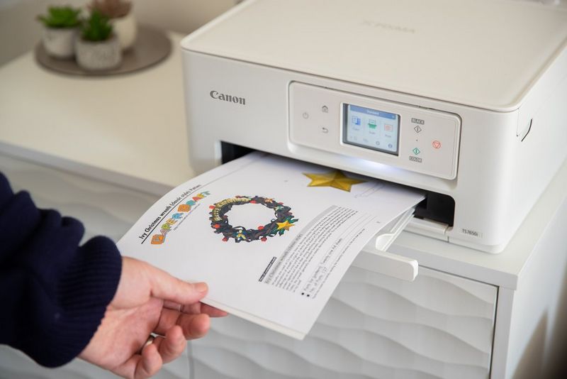 A hand reaches out to take a printout of a Creative Park festive wreath template from a Canon PIXMA printer.