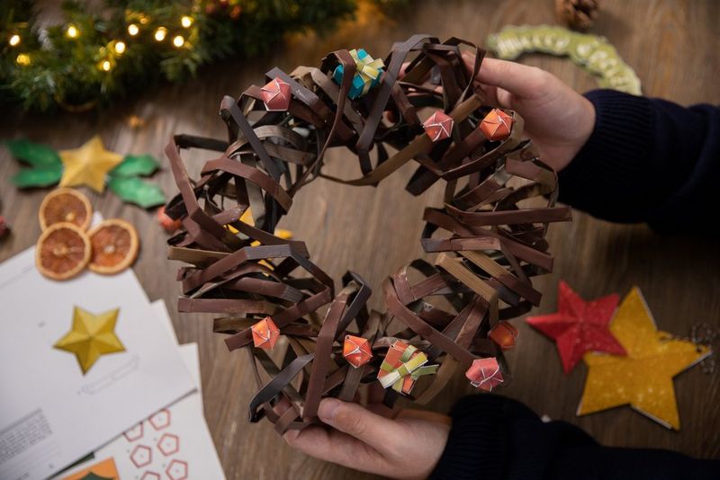 A pair of hands hold out a Creative Park papercraft wreath decorated with small papercraft Christmas presents.