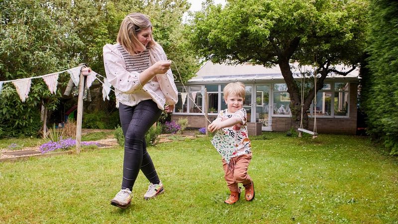 Een moeder en haar zoontje proberen een mooie papieren vlieger op te laten in hun lommerrijke achtertuin. Ze hebben plezier en lachen allebei.