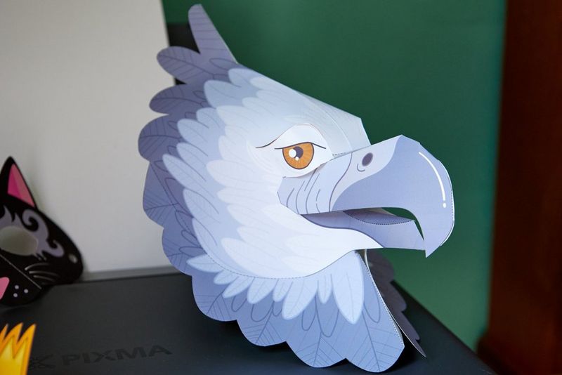 An eagle mask is positioned upright as a piece of decor, with the edge of a cat mask seen displayed to the side.