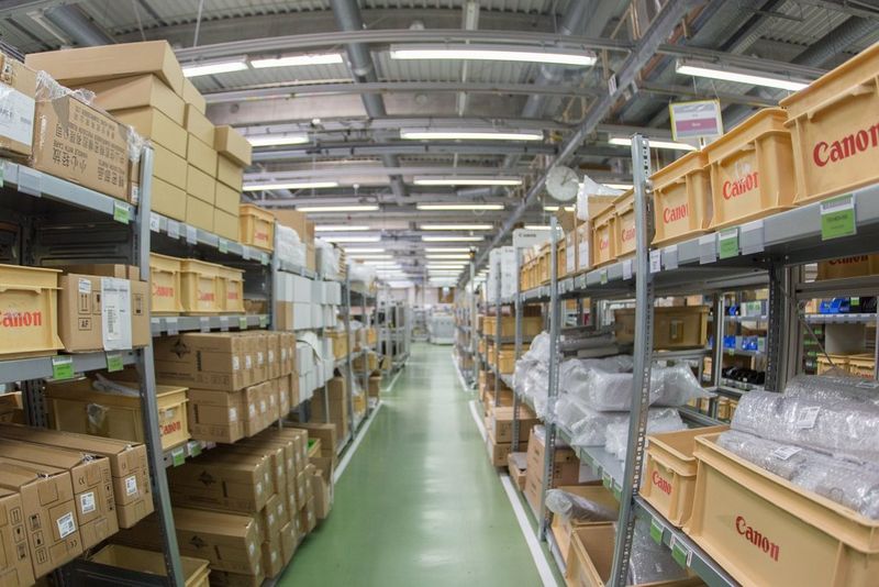 Een foto met blik op een magazijngang met aan weerszijden rijen productschappen, met zowel verticale als horizontale beeldelementen met tonvormige vertekening.