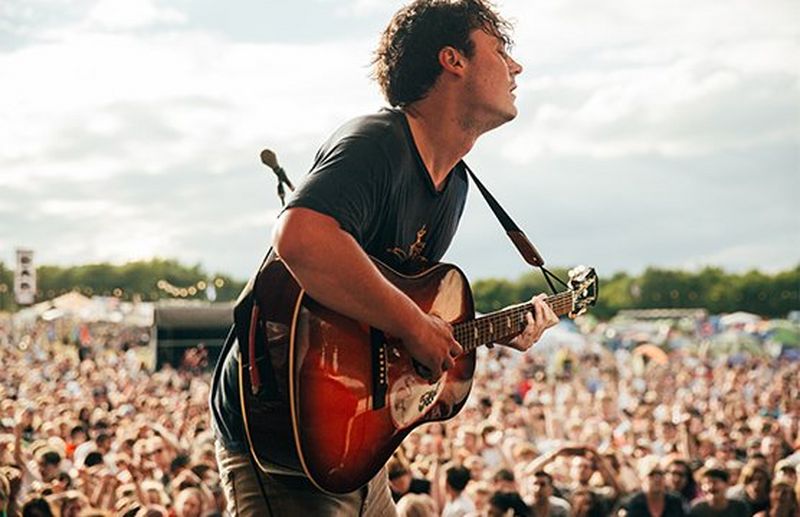 A rock musician on stage at a festival plays the guitar. Photo by Ben Morse.