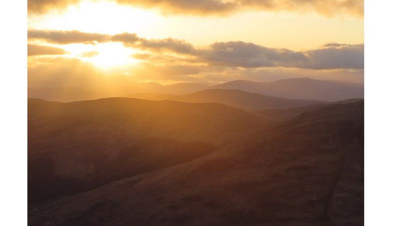 The sun sets over a low mountain landscape.