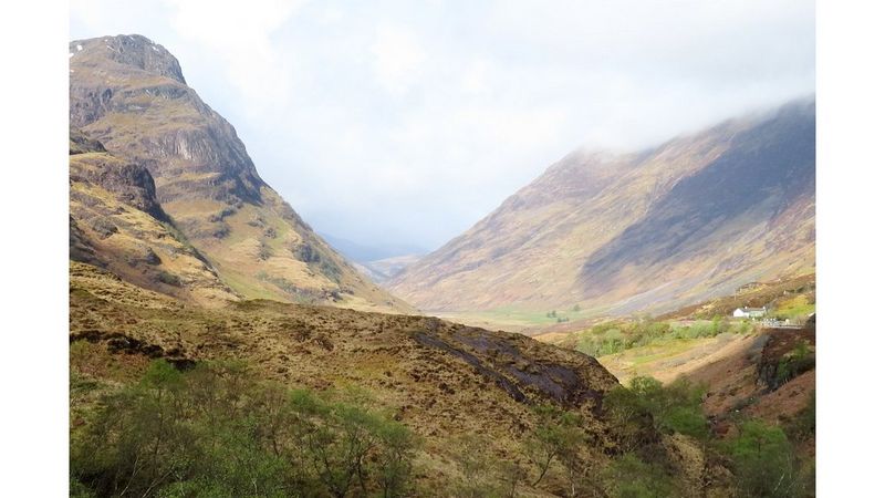 A green valley flanked with mountains stretching up into the clouds.