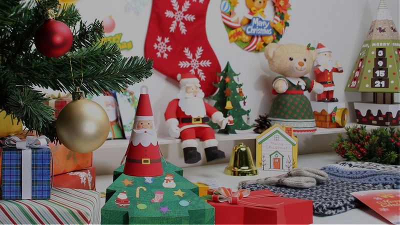 A table is filled with Christmas-themed paper crafted decorations and gifts.