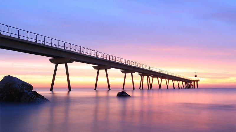 A long jetty, viewed from water level at dusk, stretches into the sea.
