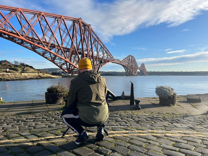 הצלם מאט דוּג מתכופף מאחורי חצובה כדי לצלם גשר באמצעות תכונת תיחום המיקוד במצלמת Canon EOS R7.