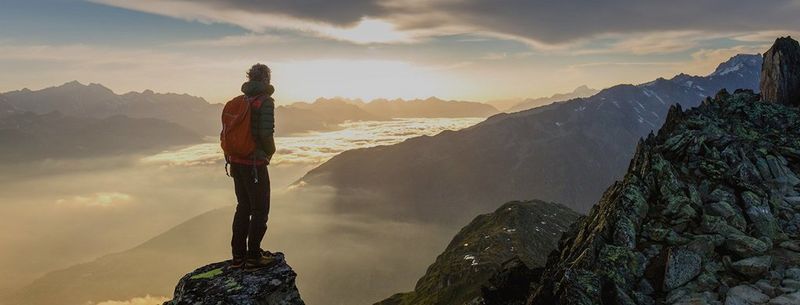 A hiker stands on top of a tall mountain at dawn