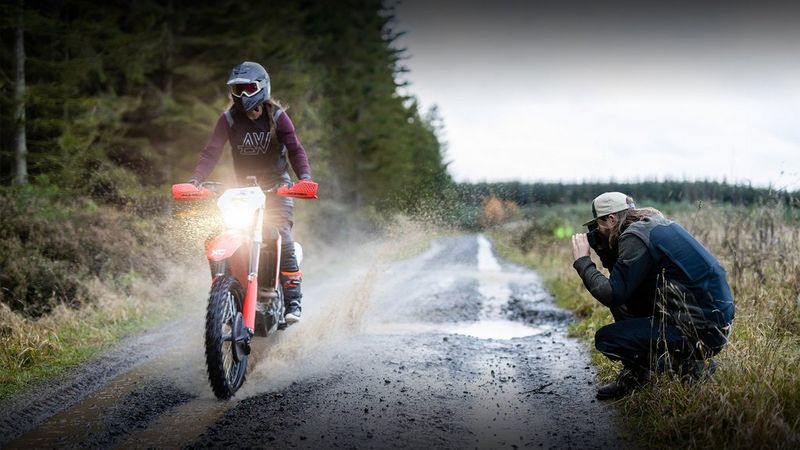 A dirt-bike speeds through a puddle, creating a spray of water.