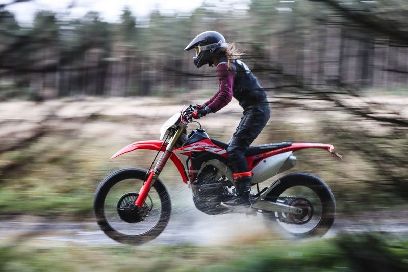 A sharp rider on a dirt-bike, with foreground branches and background scenery both blurred.