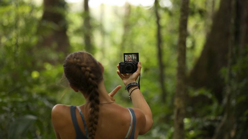 Laura Bingham pictured from behind, facing dense jungle, as she films a vlog with a Canon PowerShot G7 X Mark II.