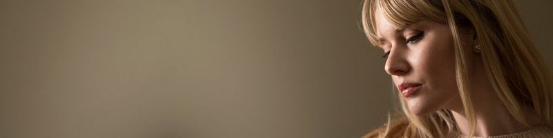 A woman against a grey wall is lit softly.