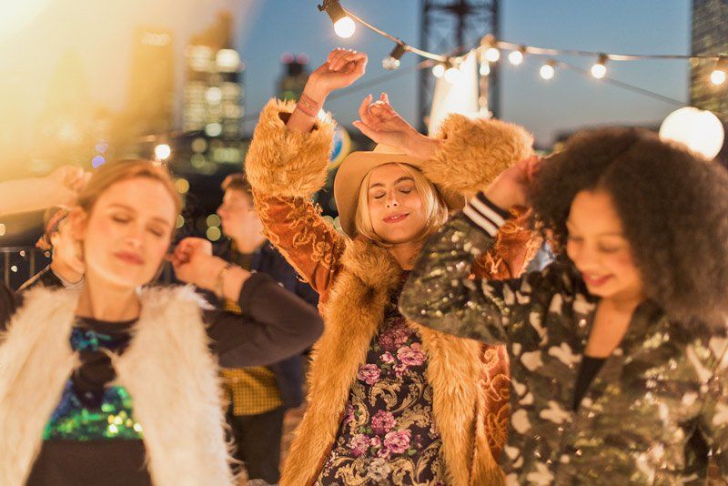 Three women are pictures dancing in a candid style, at a roof-top party.