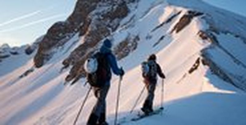 Two cross-country skiers makes their way up a mountain in low sunlight.